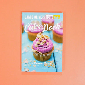 The Cake Book by Cupcake Jemma featuring a cupcake with pink frosting on a blue wooden surface.